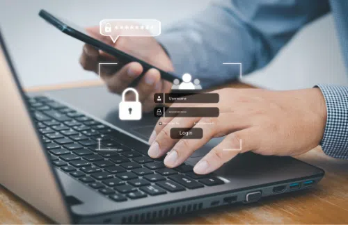 Person using a smartphone and typing on a laptop keyboard with a graphic overlay of a login screen and security icons representing account login and data protection.