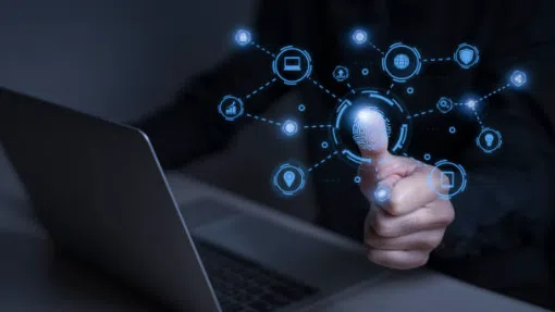 A person using a laptop touches a digital fingerprint icon, surrounded by security and technology symbols, suggesting biometric authentication.