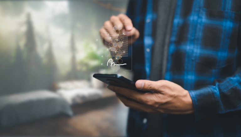 A person uses a smartphone with a digital signature interface projected above the device; a blurred room background is visible.
